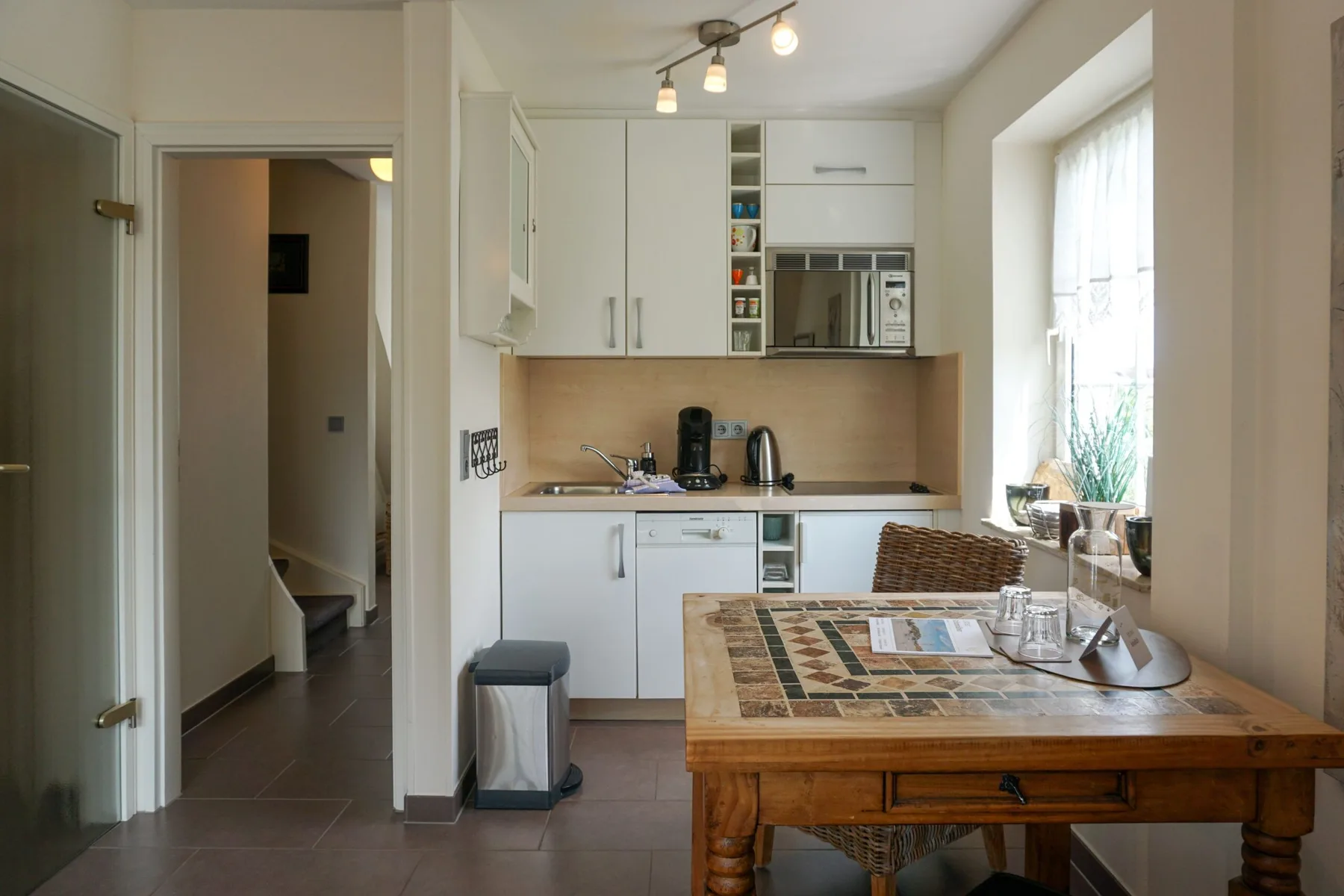 A bright kitchen and dining area with white cabinets, a wooden table, and a large window.