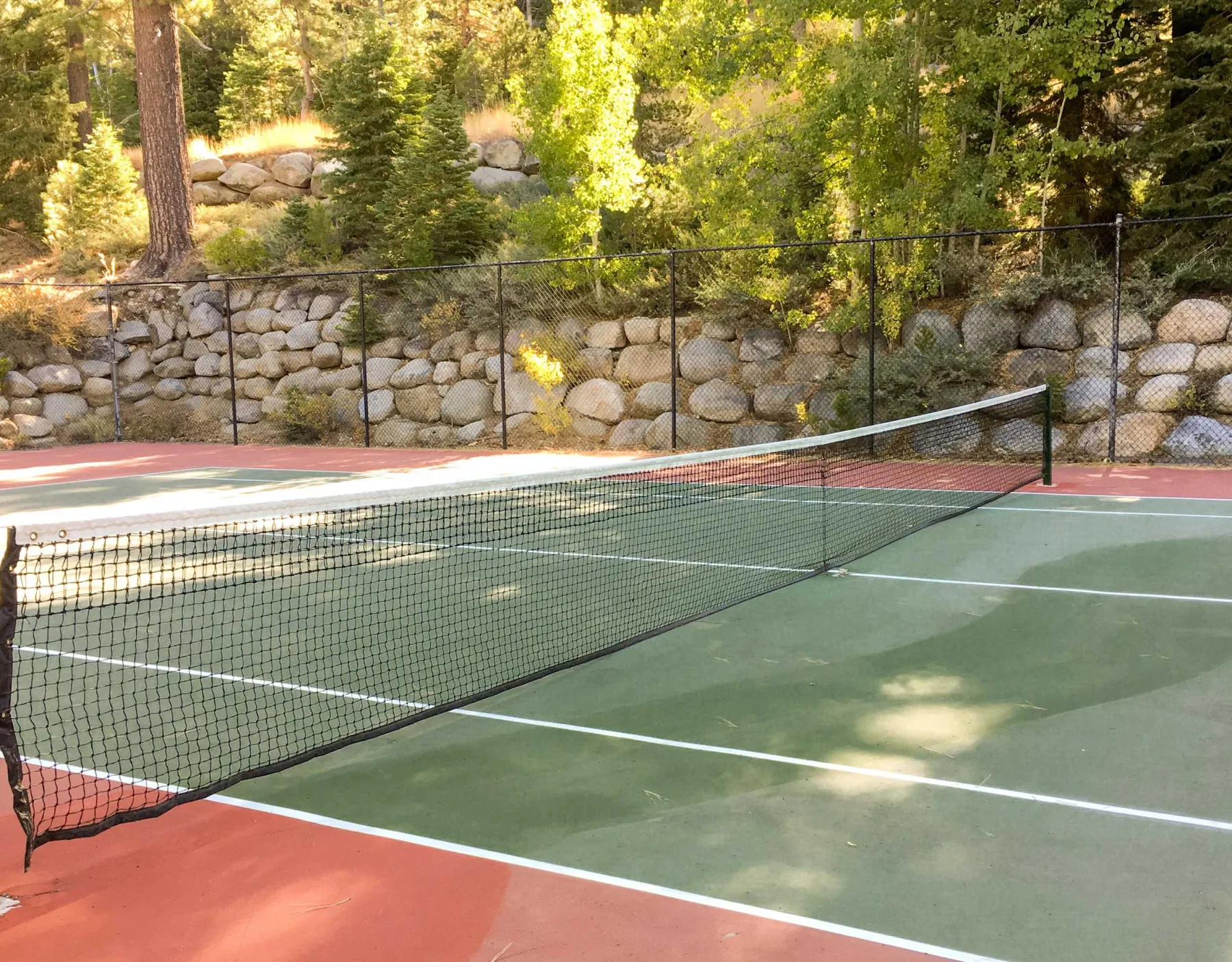 Shared amenity: Outdoor tennis court with a net, surrounded by trees and a stone retaining wall.