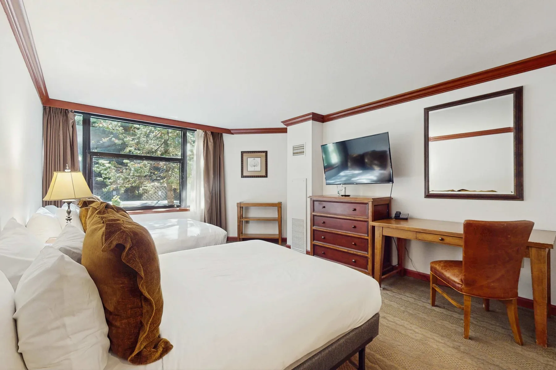 A bedroom with two beds, a window, and a desk with a television.