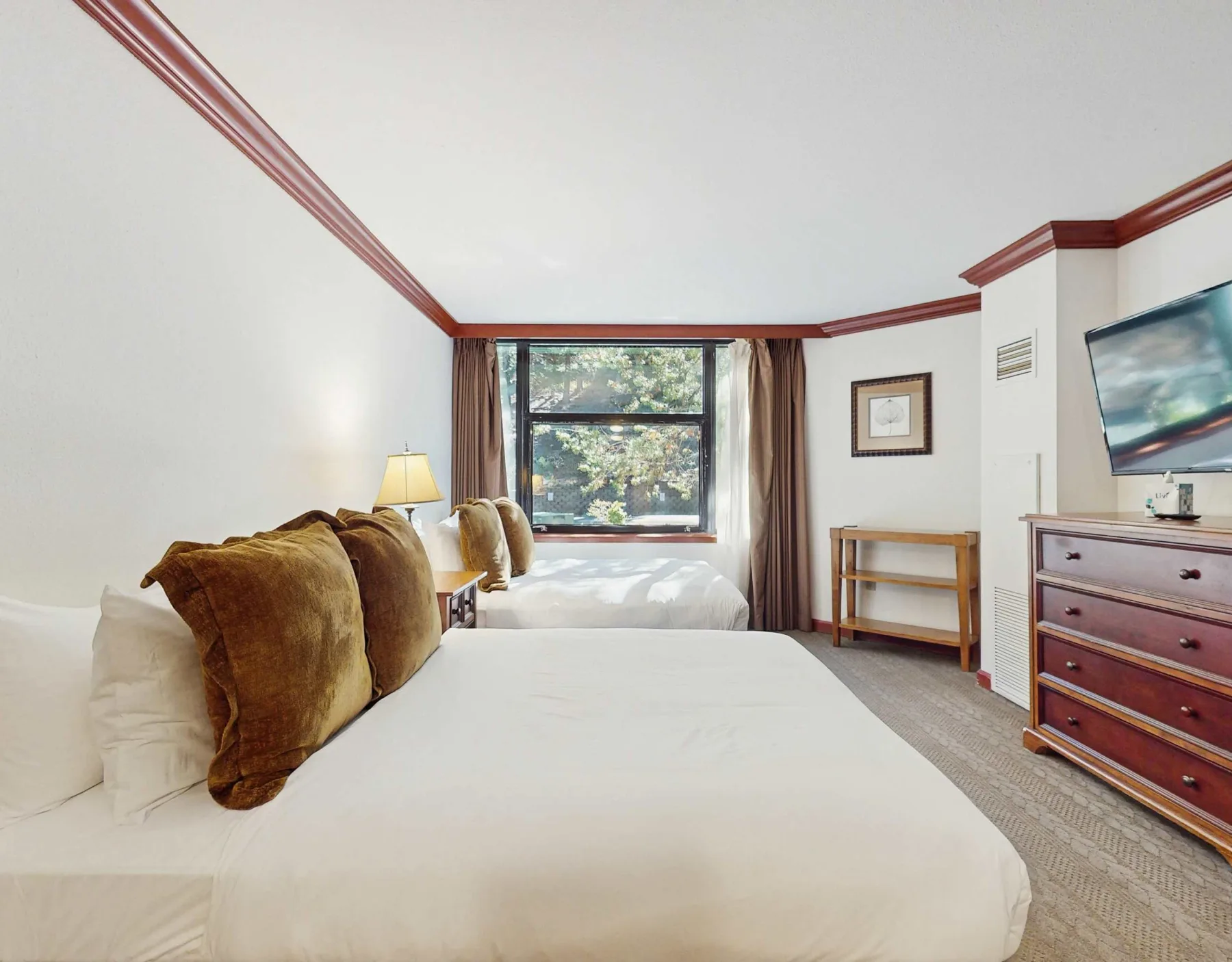 A bedroom with two beds and a large window overlooking trees.
