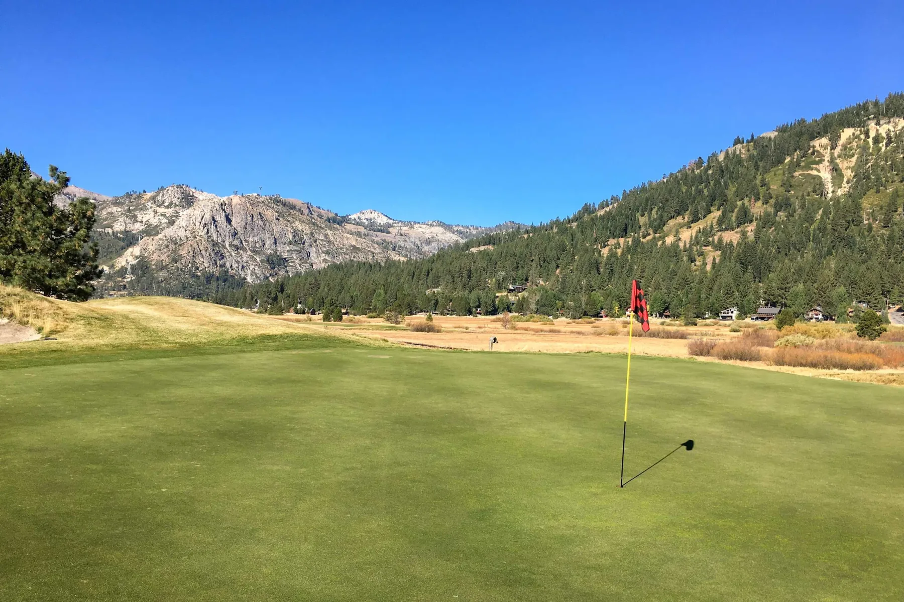 Shared amenity: A golf course green with a flag, backed by forested hills and mountains.