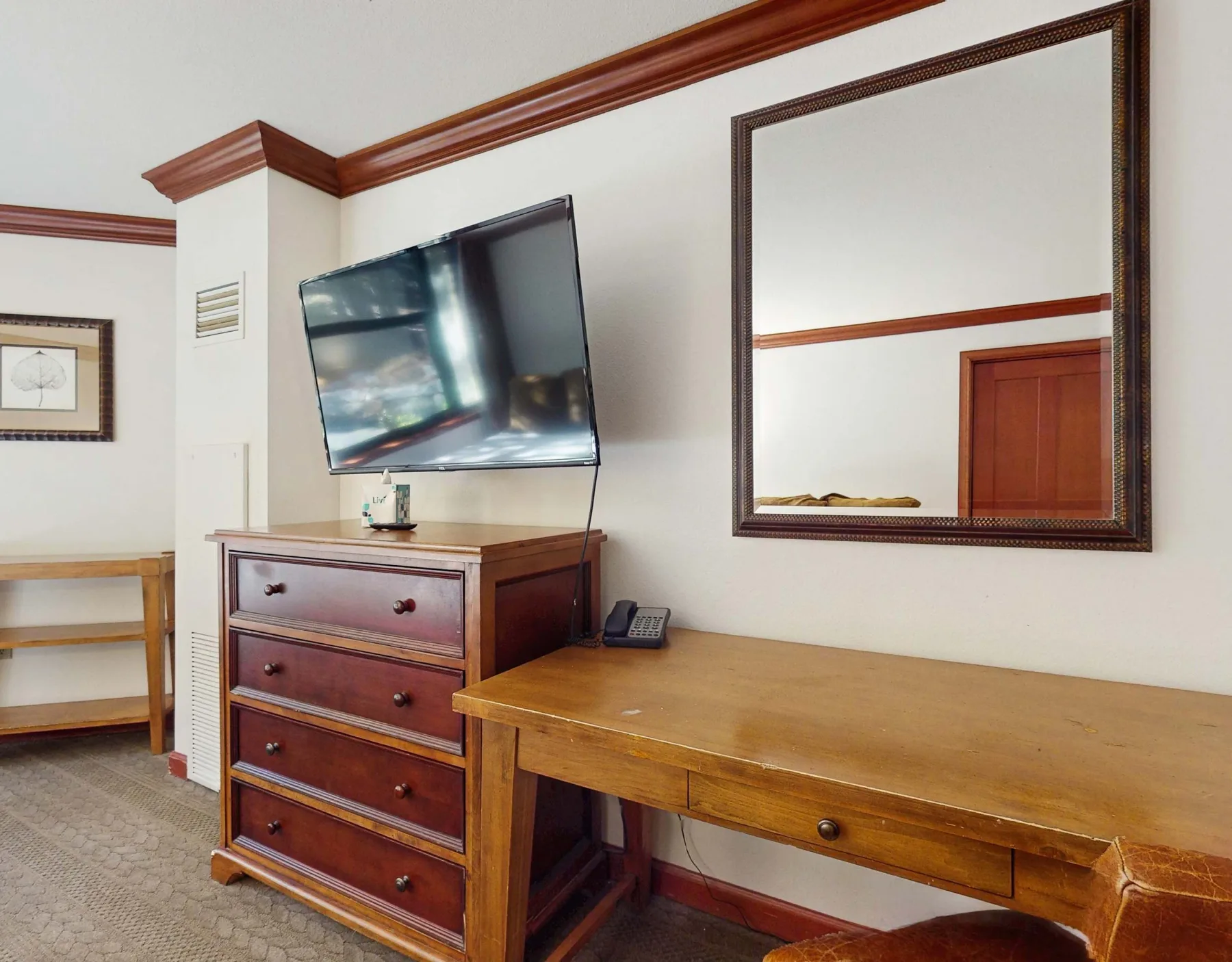 A bedroom corner with a television, wooden dresser, and desk.