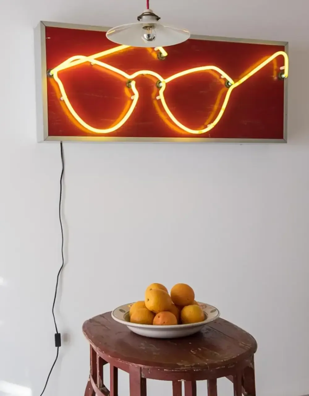 Representative hotel space: A room features a glowing glasses-shaped wall sign above a small table with fruit.