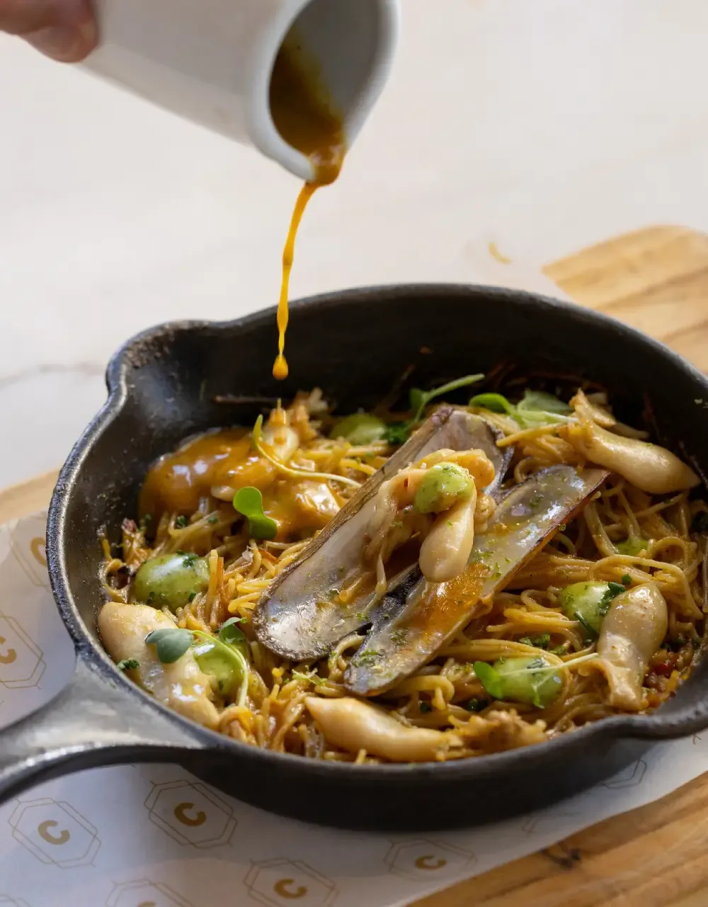 Representative hotel space: A skillet of noodles and vegetables is being drizzled with sauce.