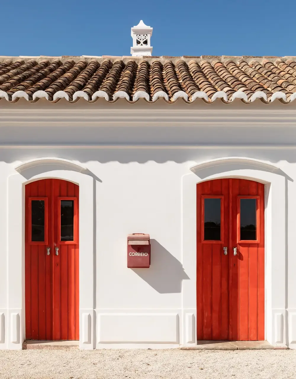 Representative hotel space: A white building facade has two red doors beneath a tiled roof.