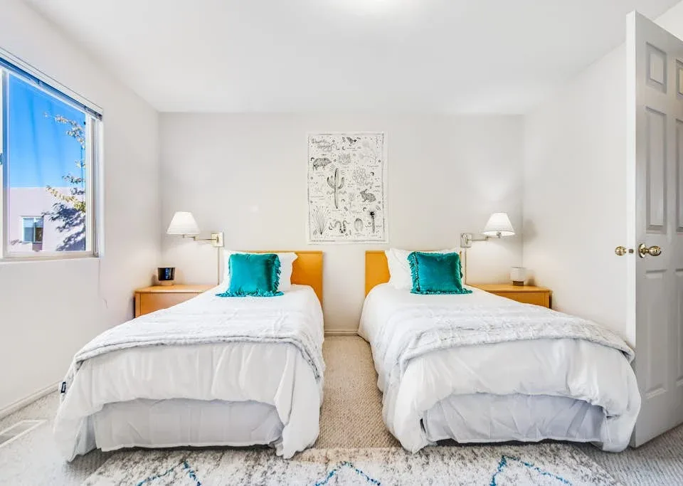 A bright bedroom with two single beds and teal accent pillows.