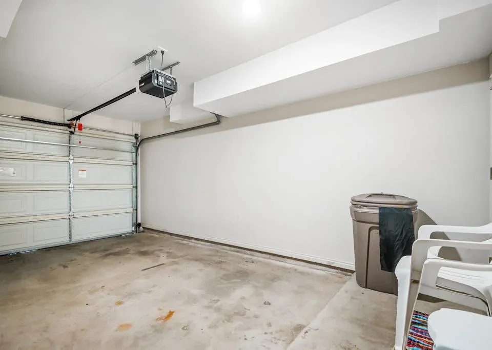 An empty garage with a closed overhead door, a storage bin, and stacked chairs.