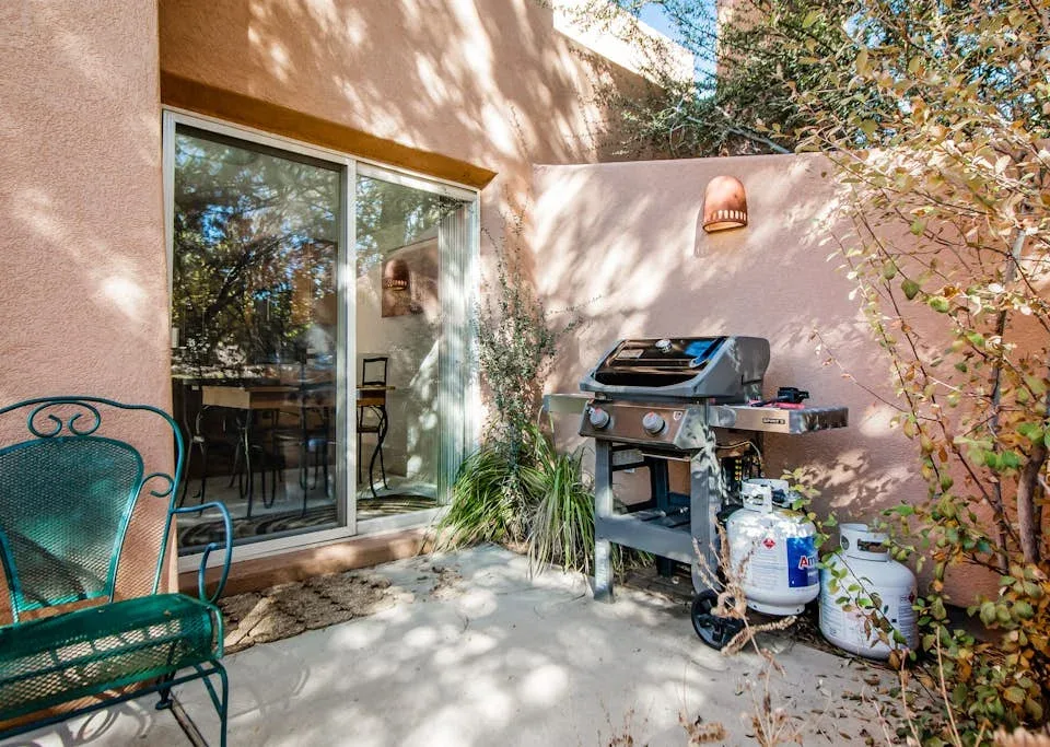 A patio with a barbecue grill beside a sliding glass door and outdoor seating.