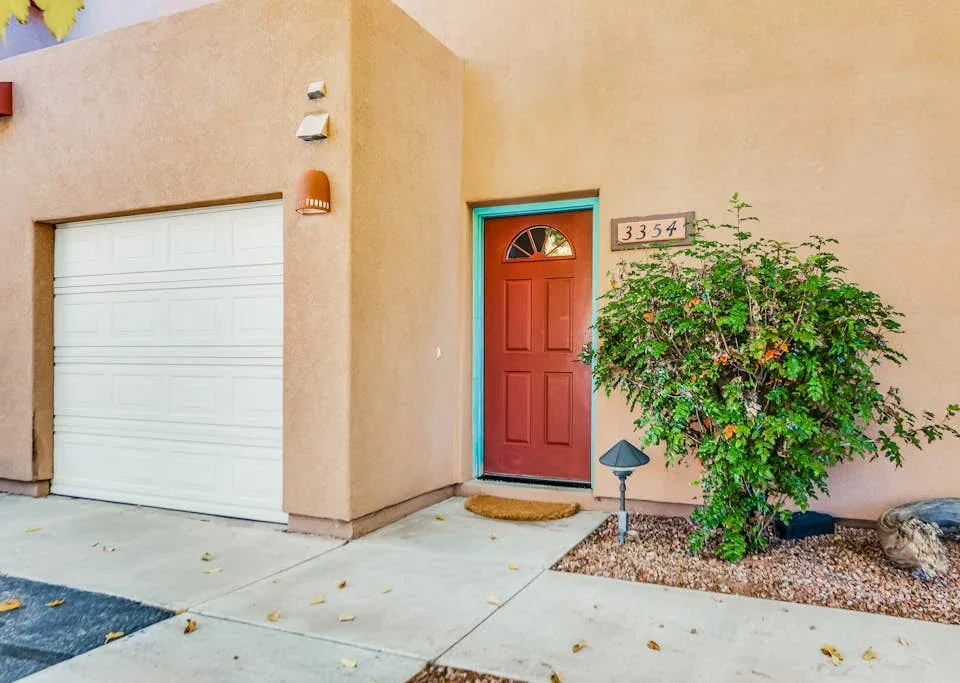 A peach-colored house facade with a red front door and a leafy shrub.