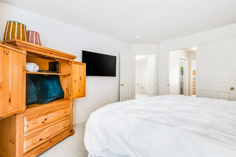 A bright bedroom with a large bed and wooden dresser.
