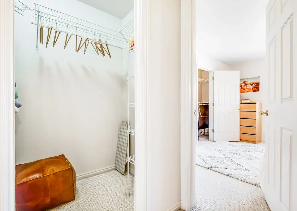 A bright closet with hanging clothes rails opens onto a bedroom.