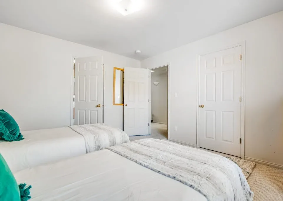 A bedroom with two beds and white bedding.