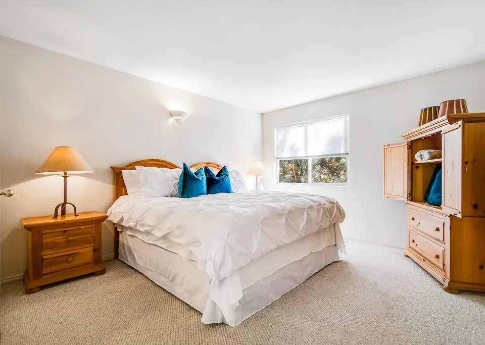 A bright bedroom features a bed with white bedding and a window.
