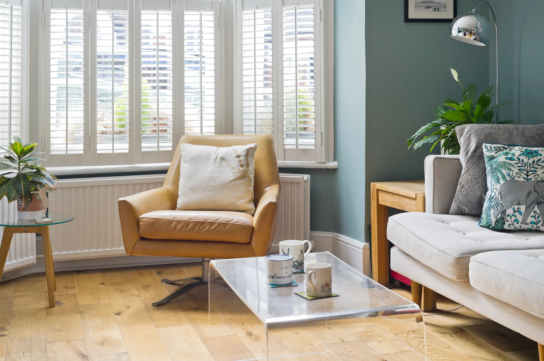 Una sala de estar con un sillón y un sofá junto a grandes ventanas con persianas.