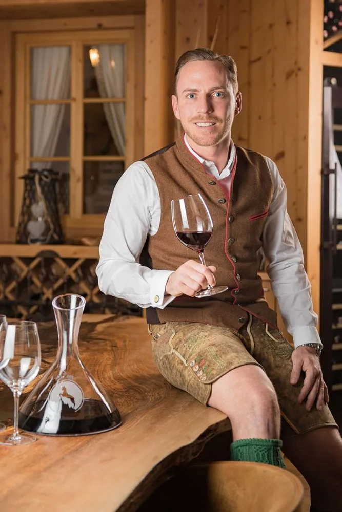 Representative hotel space: A man in traditional-style clothing sits at a wooden table holding a glass of wine.