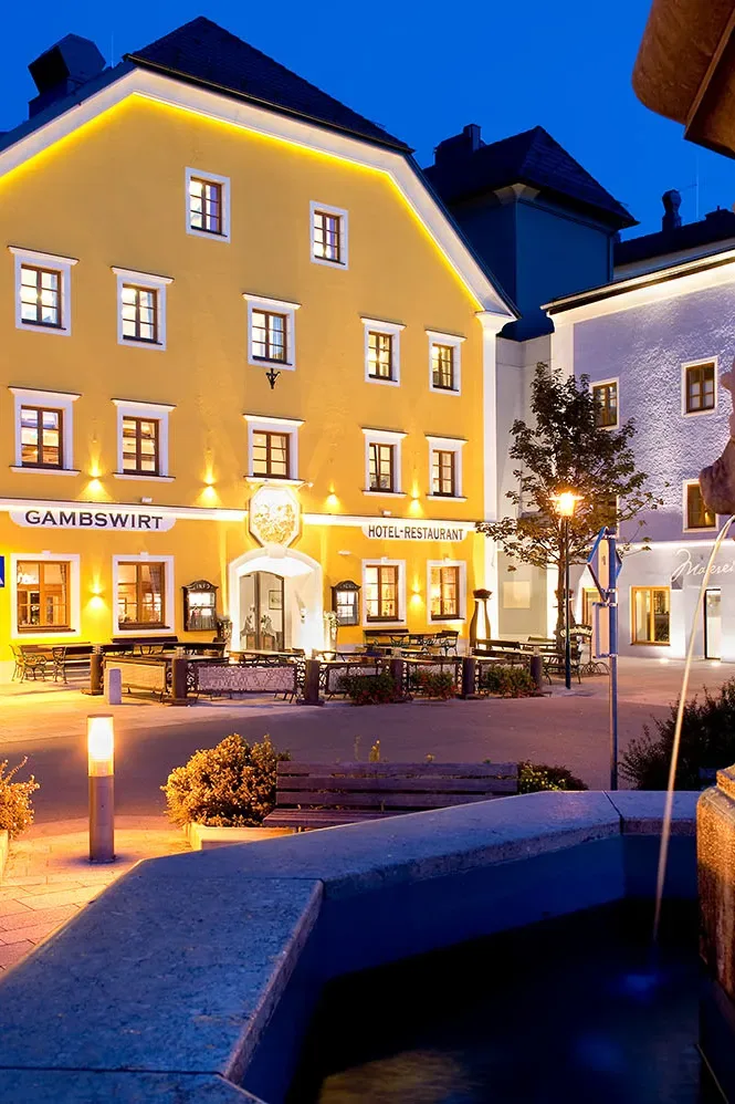 Representative hotel space: A brightly lit hotel facade faces a paved courtyard at dusk.