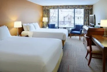 Representative hotel space: A hotel bedroom with two beds, a desk, and windows overlooking nearby buildings.
