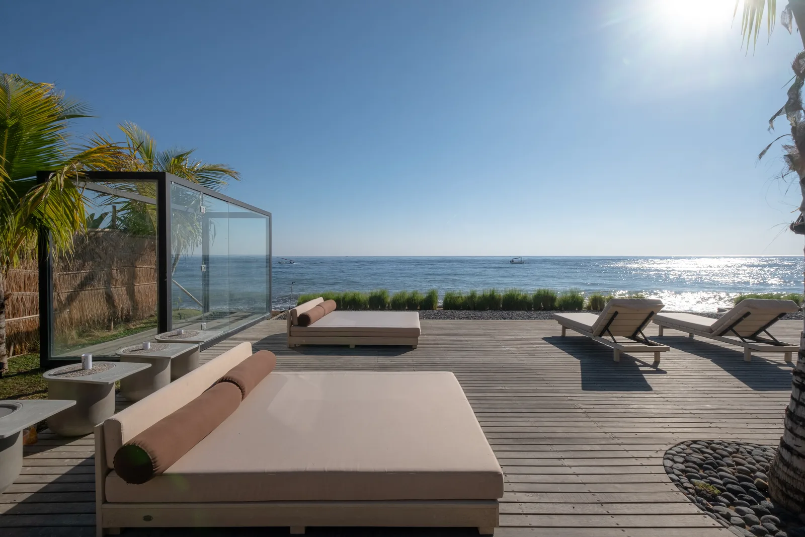 Zona común: Una terraza junto al mar con tumbonas acolchadas y una barandilla de vidrio da al océano.