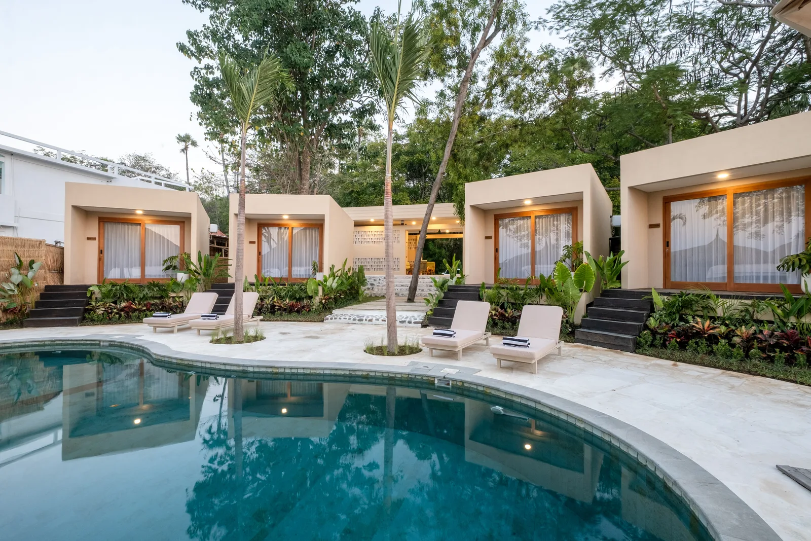 Zona común: Zona de piscina al aire libre con asientos junto a habitaciones ajardinadas.