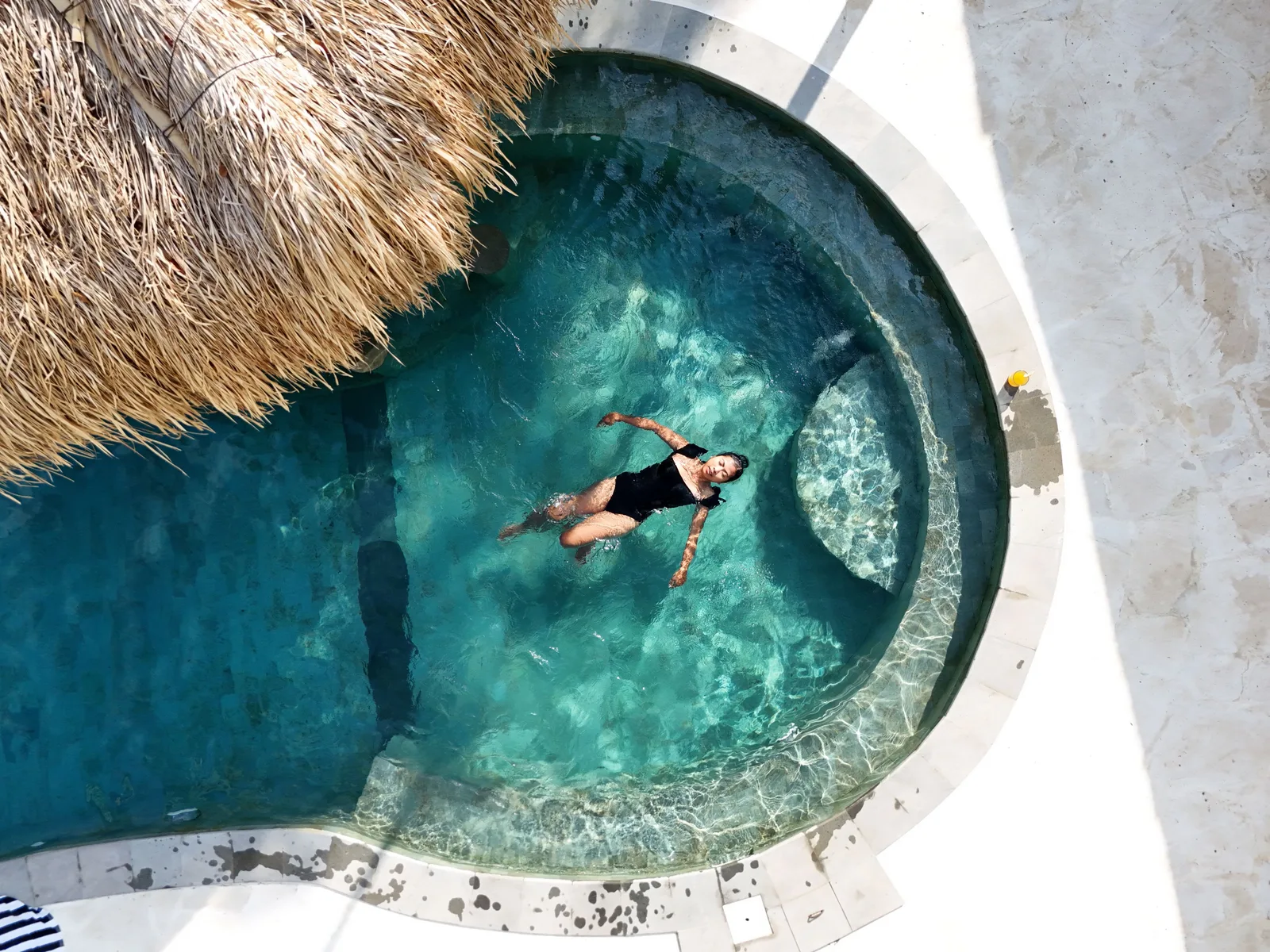 Zona común: Una persona flota en una piscina curva junto a un techo de paja.