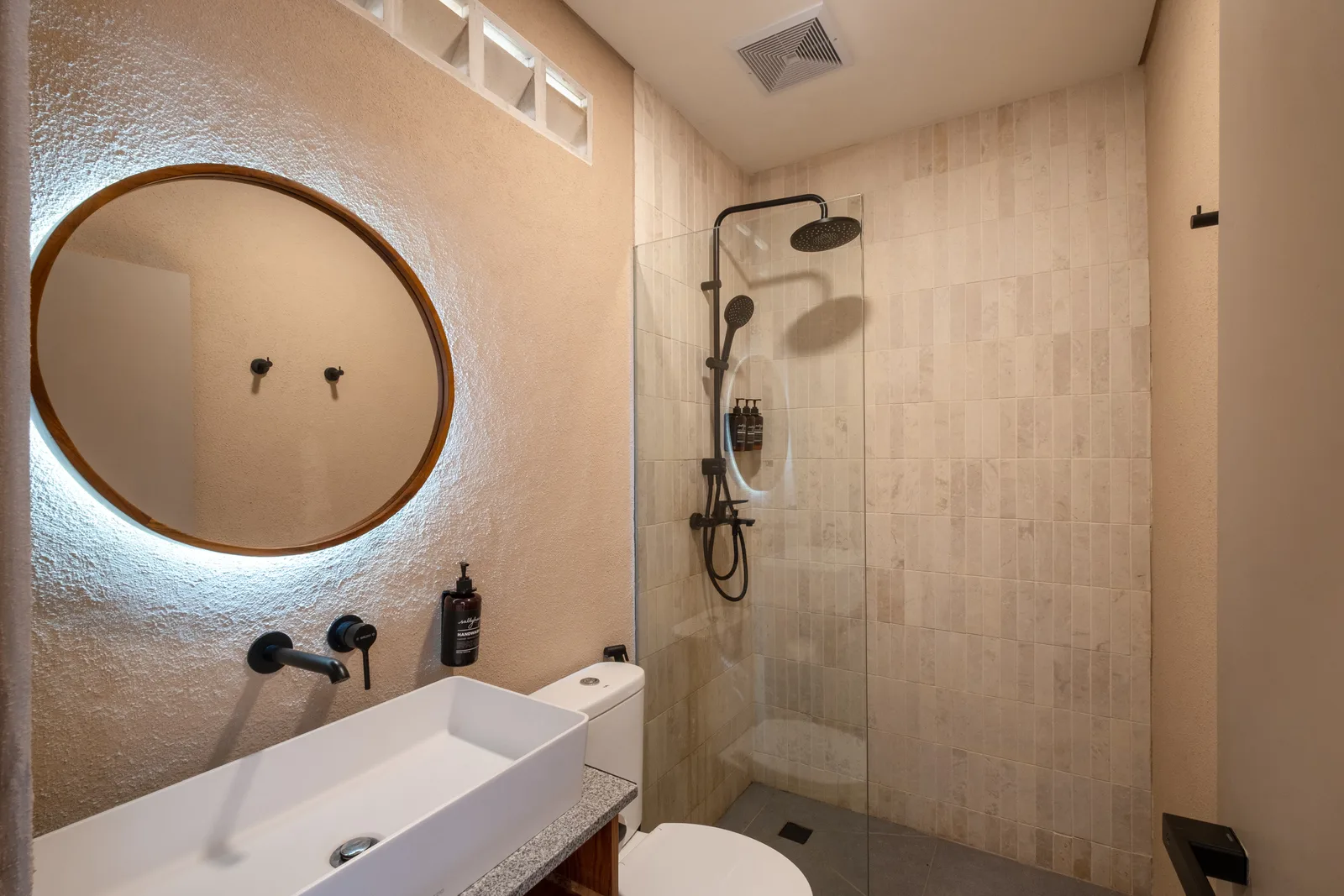 Un baño con lavabo, espejo redondo y ducha de vidrio.