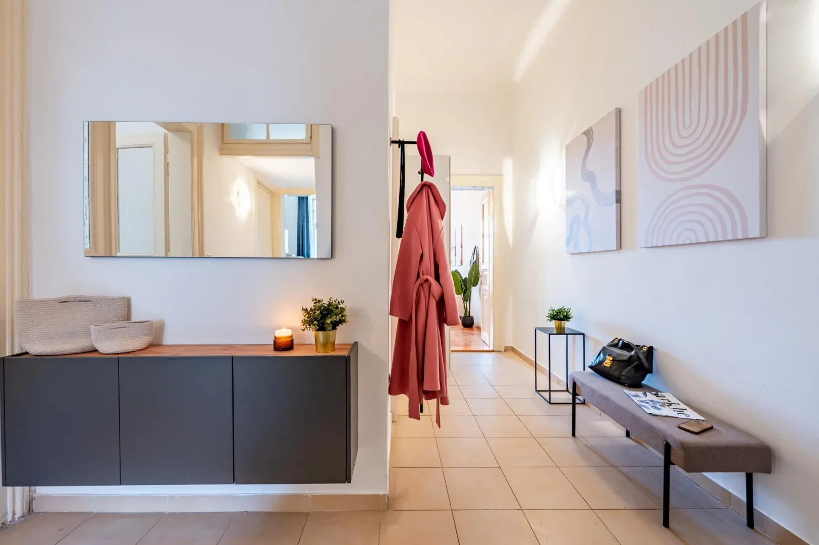 A bright entryway with a dark cabinet, wall mirror, coat rack, and cushioned bench beneath abstract art.