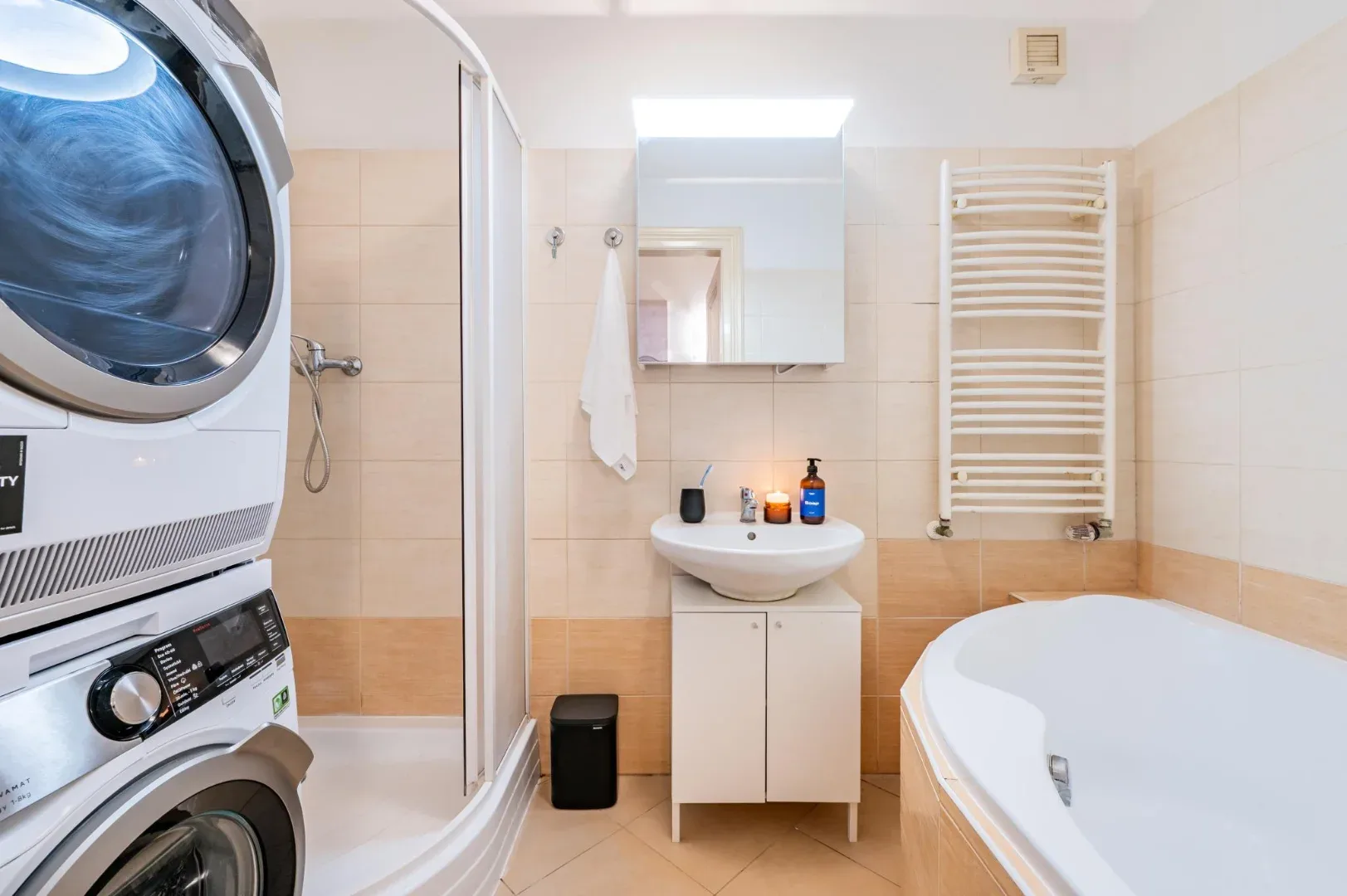 A tiled bathroom has a sink and mirror, a shower enclosure, a heated towel rail, and a bathtub.