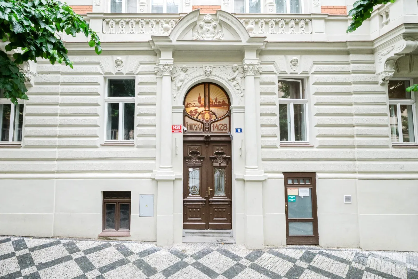 Shared amenity: An ornate white building facade has a carved entrance, dark wooden double doors, and patterned stone pavement.