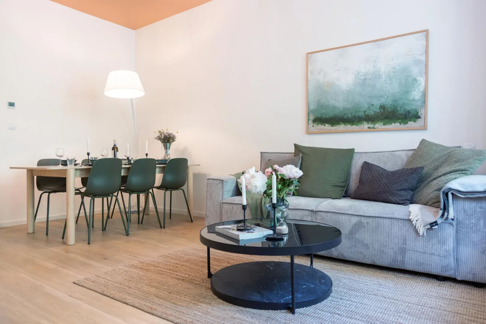 A living and dining area with a gray sofa, round coffee table, and dining table beneath a hanging lamp.