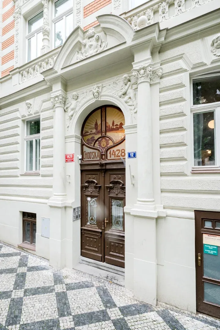 Shared amenity: Ornate building entrance with carved white stonework, a dark wooden double door, and patterned pavement.