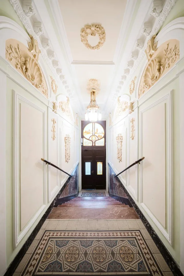 Shared amenity: An ornate hallway with decorative plasterwork, patterned floor tiles, and a dark entrance door.