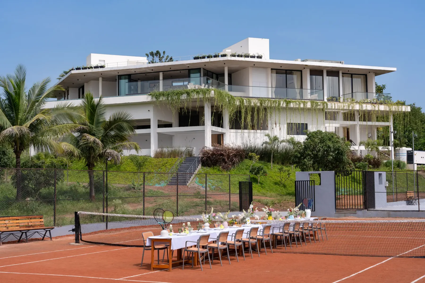 Un edificio moderno da a una cancha de tenis al aire libre con una larga mesa preparada.