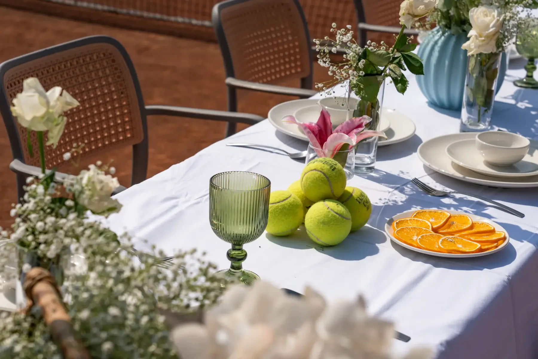 Una mesa puesta con cítricos, flores, platos y vasos.