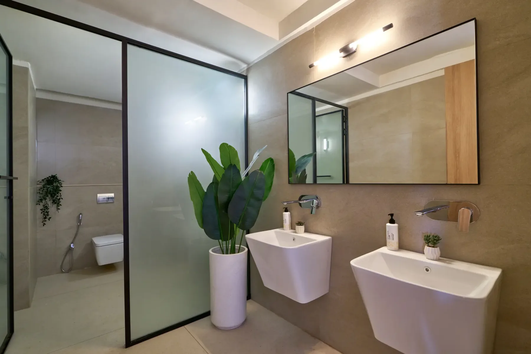 Un baño moderno con dos lavabos blancos, un espejo grande y una planta en maceta.