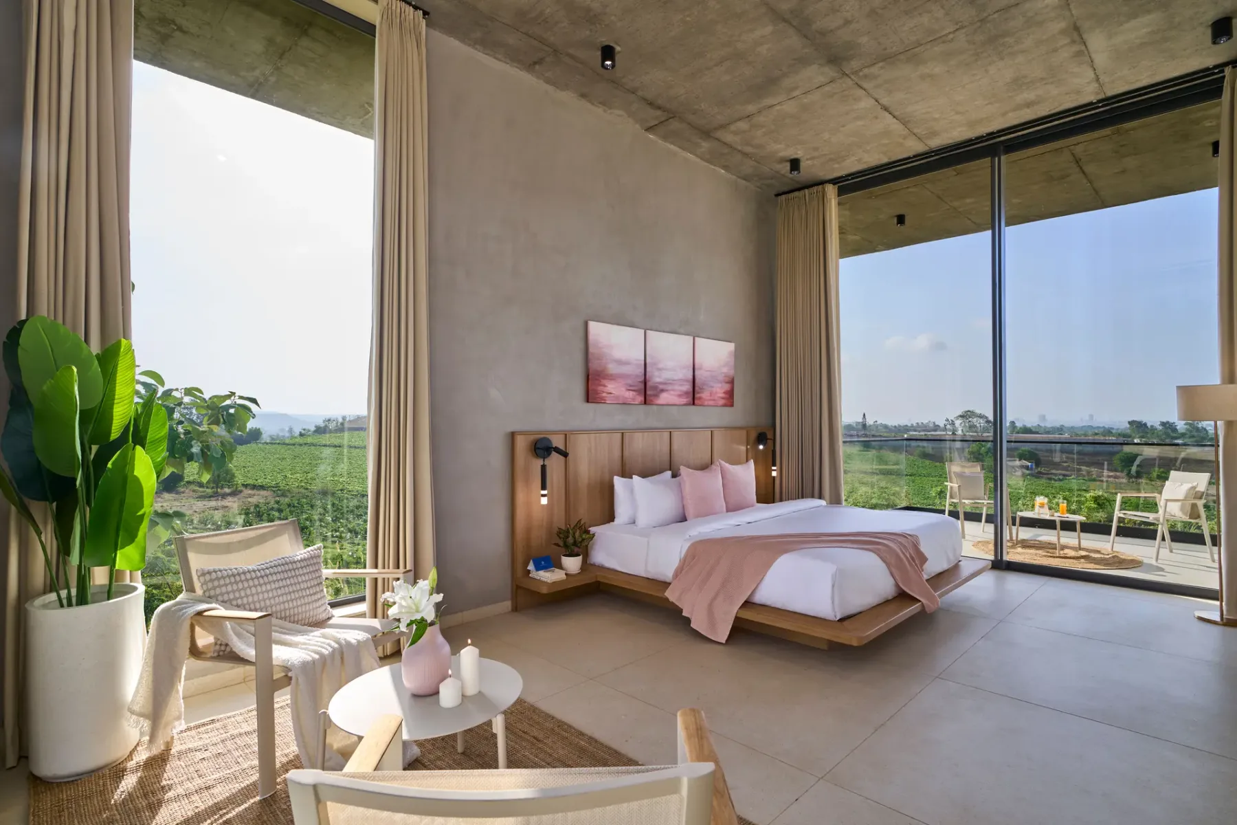 Un dormitorio con cama y asientos junto a grandes ventanales con vistas a la vegetación.