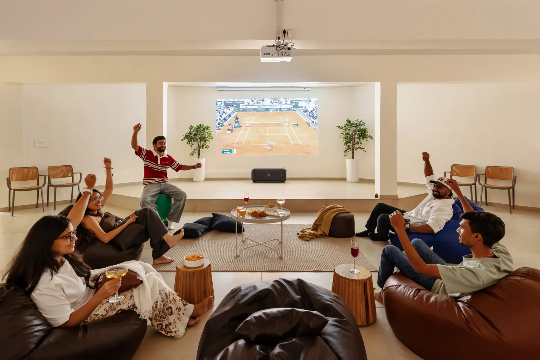 Un grupo se reúne en una sala para ver un partido de tenis proyectado en la pared.