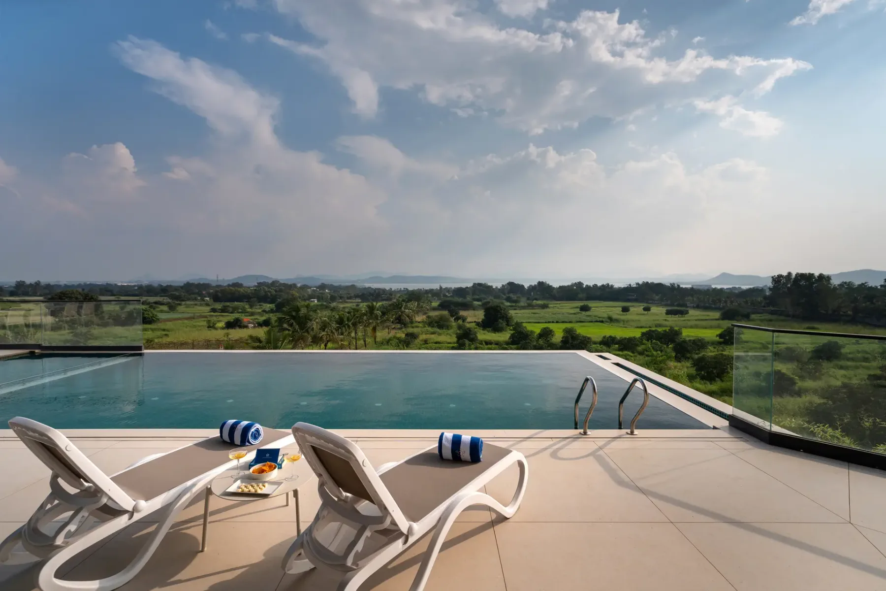Una piscina al aire libre tiene vistas a campos verdes bajo un cielo parcialmente nublado.