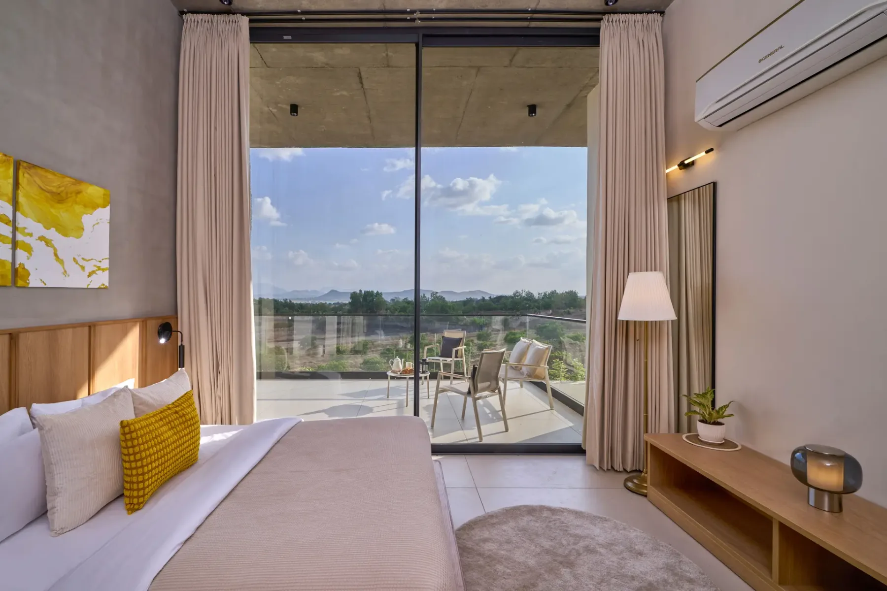 Un dormitorio se abre a un balcón mediante grandes puertas de vidrio, con asientos en el exterior.