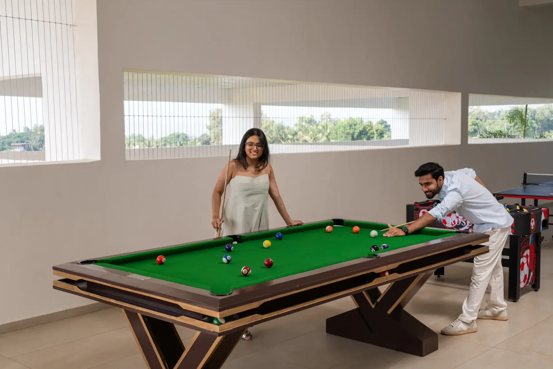 Una mesa de billar con paño verde está en una sala recreativa luminosa.