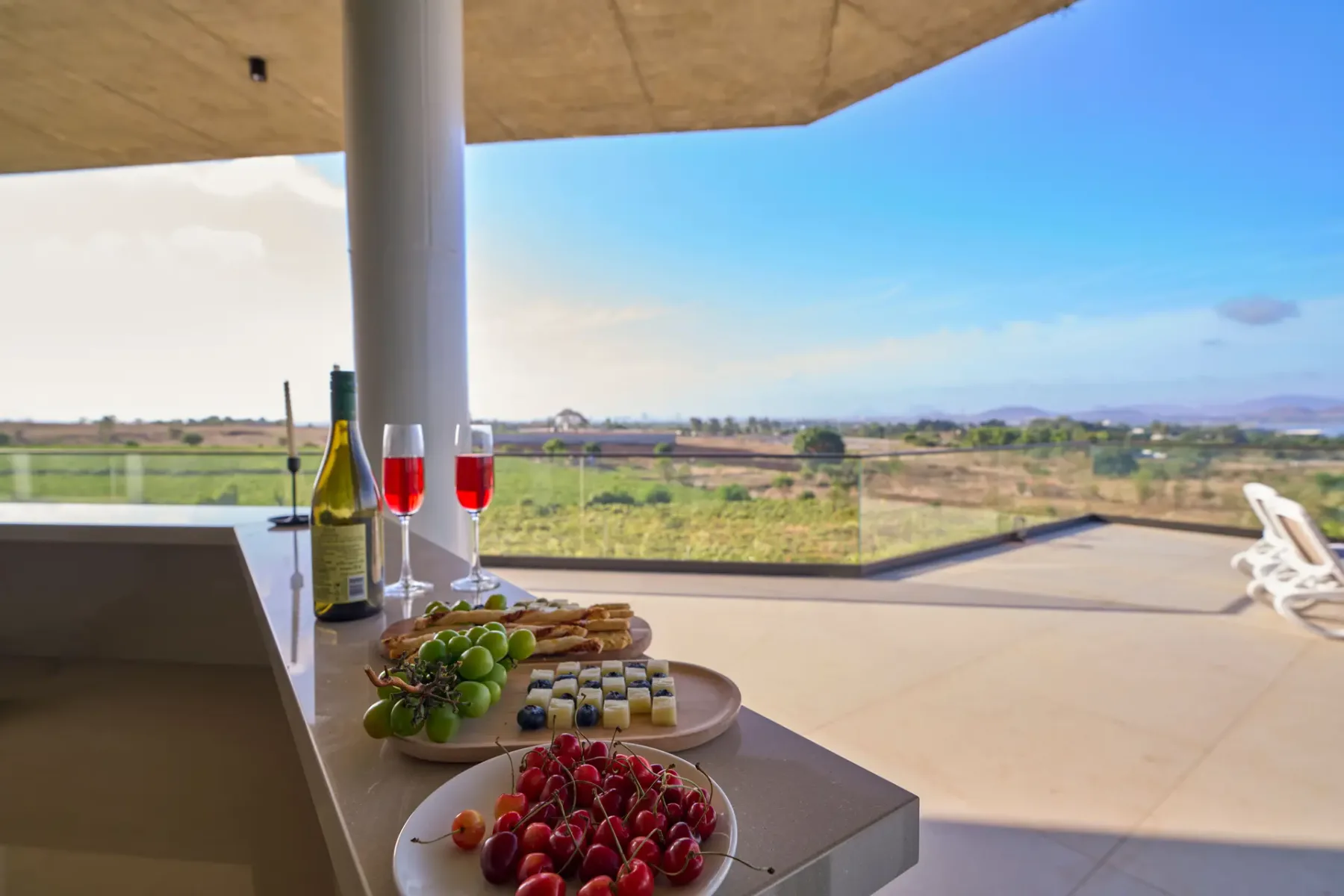 Una terraza exterior cubierta da a un paisaje rural, con fruta y bebidas sobre una mesa.