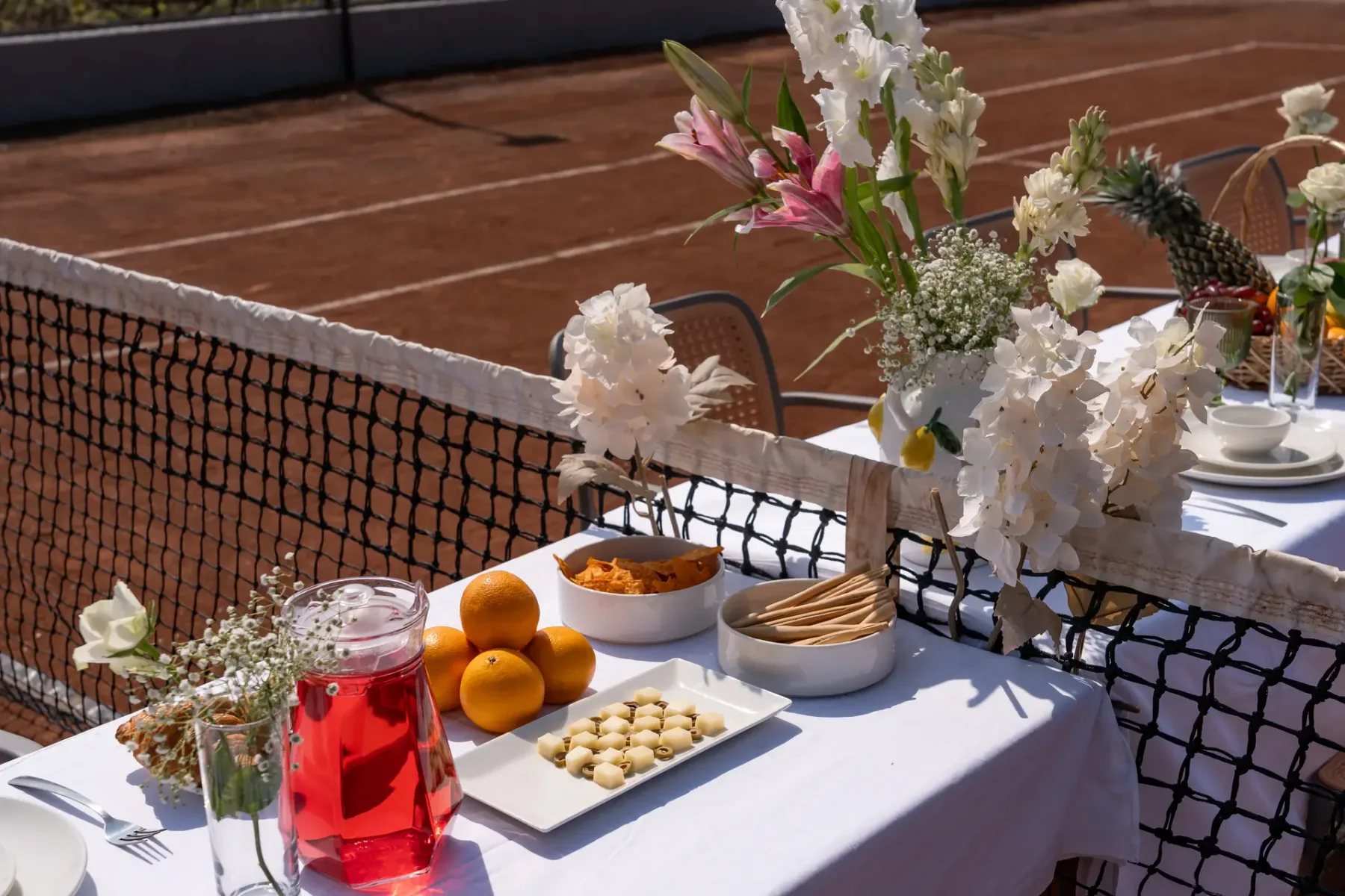 Una mesa decorada con flores y refrigerios está junto a una cancha de tenis.