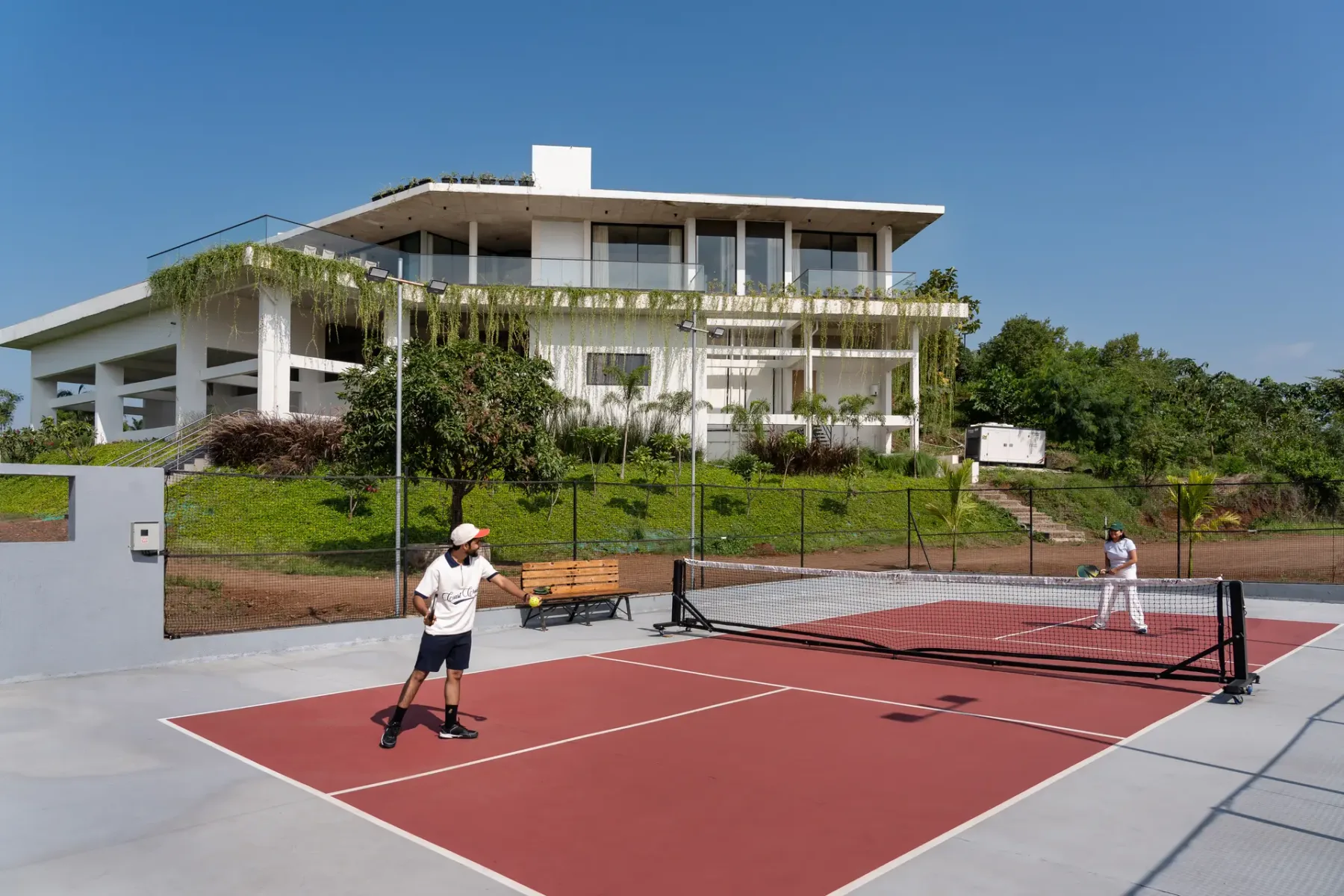 Una cancha de tenis roja está frente a un edificio blanco moderno.