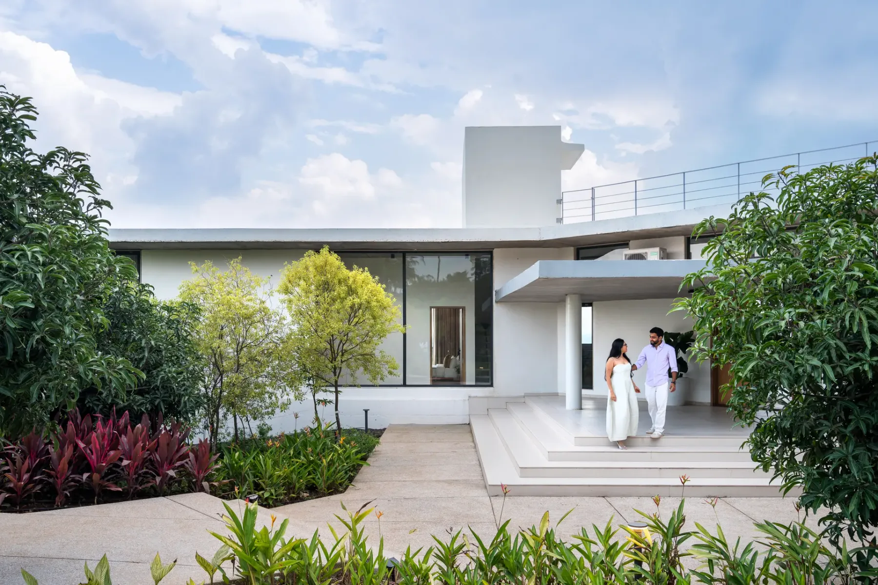 La entrada de una casa moderna da a un jardín con dos personas en los escalones.