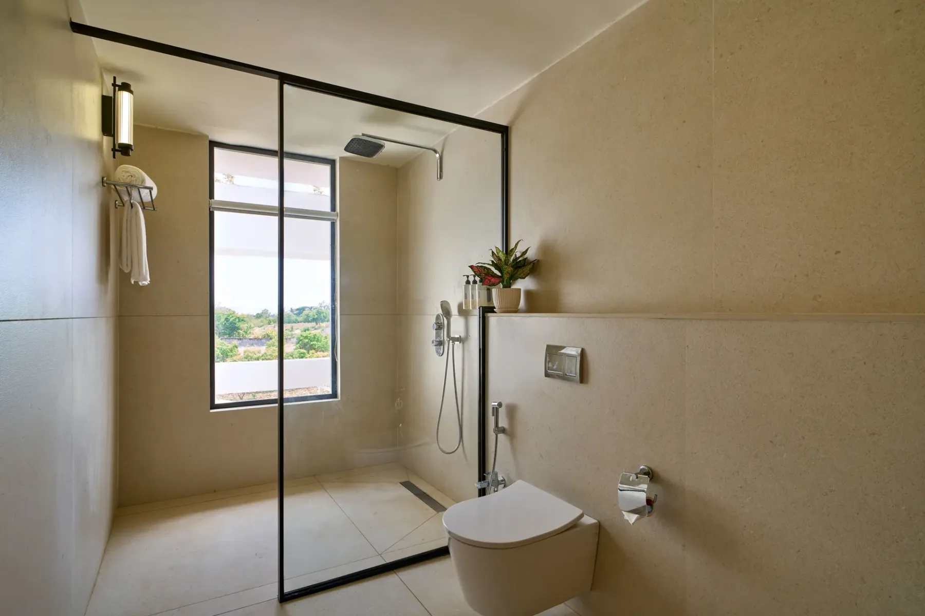 Un baño con ducha de vidrio, inodoro suspendido y ventana.