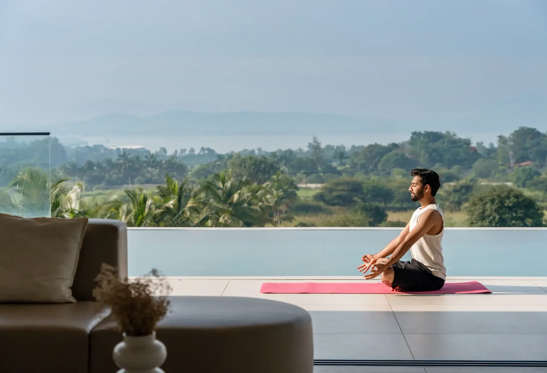 Una persona está sentada sobre una esterilla de yoga junto a una piscina, con vegetación al fondo.