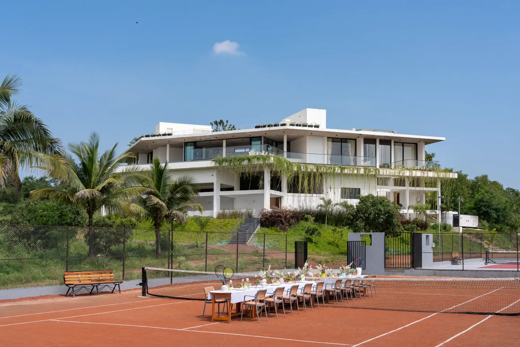 Un edificio moderno da a una cancha de tenis de arcilla con asientos en el borde.