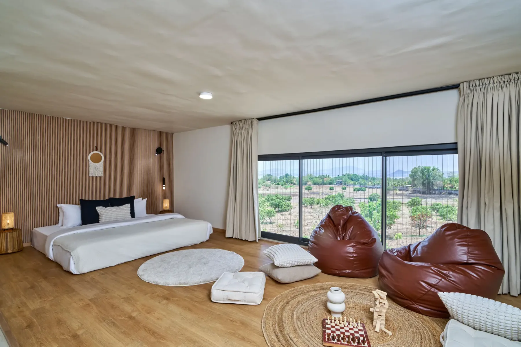 Un dormitorio con una cama baja y asientos tipo puff junto a una gran ventana.