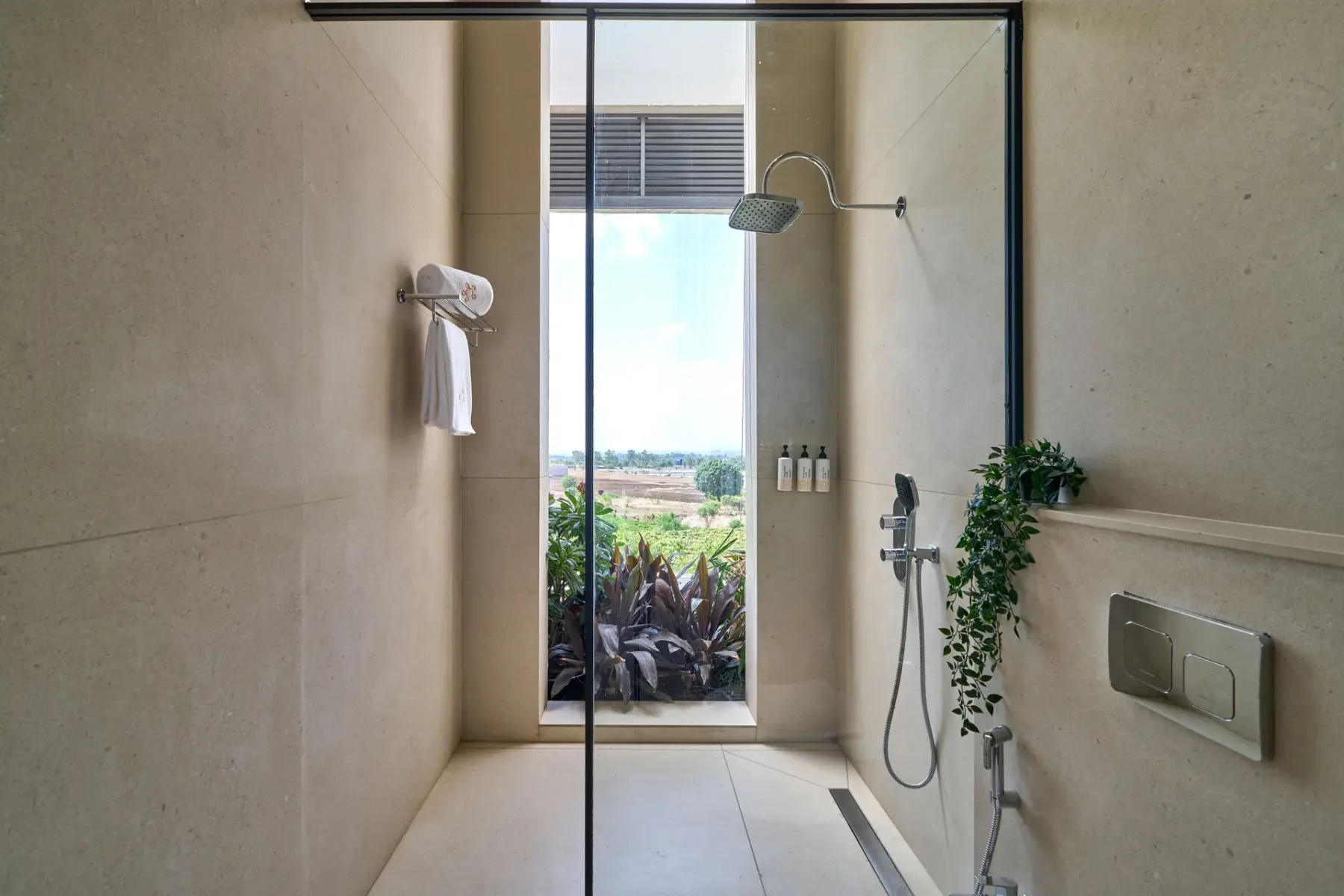 Un baño alicatado con ducha de vidrio y una ventana grande con vistas a la vegetación.