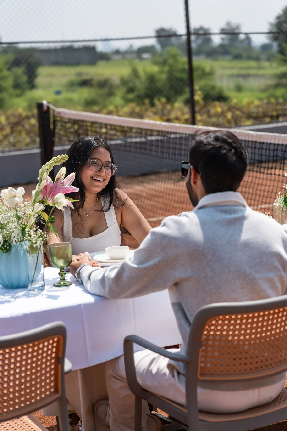 Una pareja comparte una comida en una mesa al aire libre junto a una cancha cercada.
