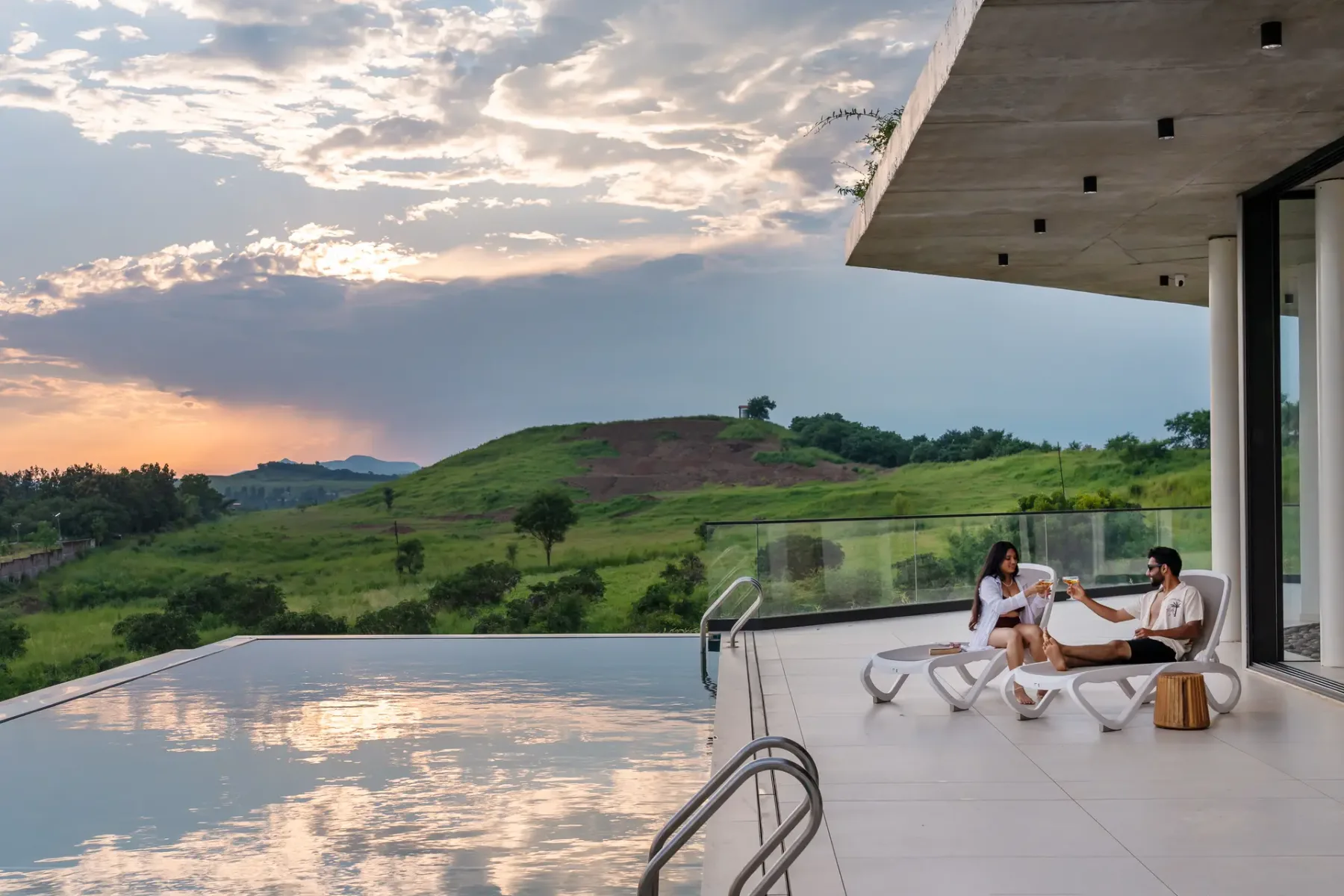 Una piscina exterior junto a un edificio moderno mira hacia colinas verdes al atardecer.